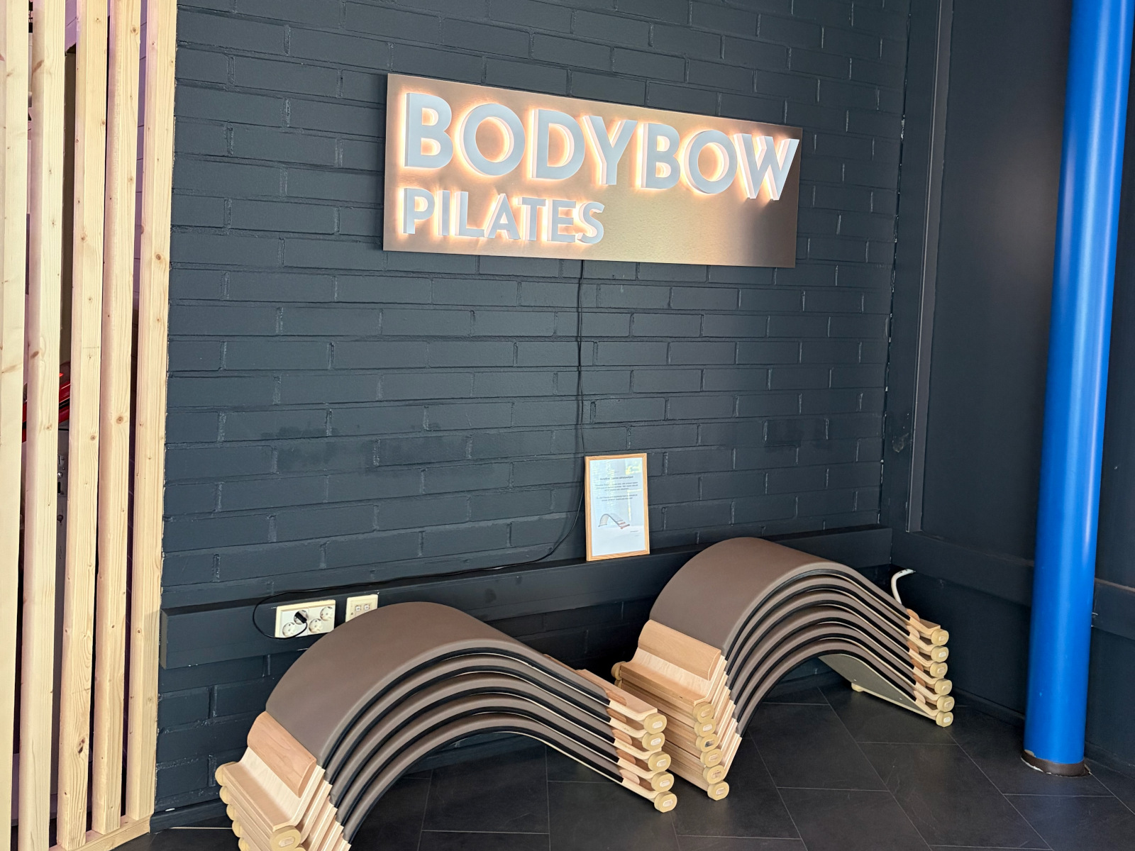 BODYBOW Pilates -valomainos tummalla tiiliseinällä